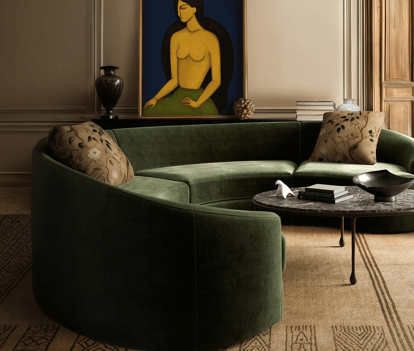 A curved, dark green velvet sectional sofa with patterned pillows, a round marble coffee table, and a large painting of a woman in a richly decorated living room.