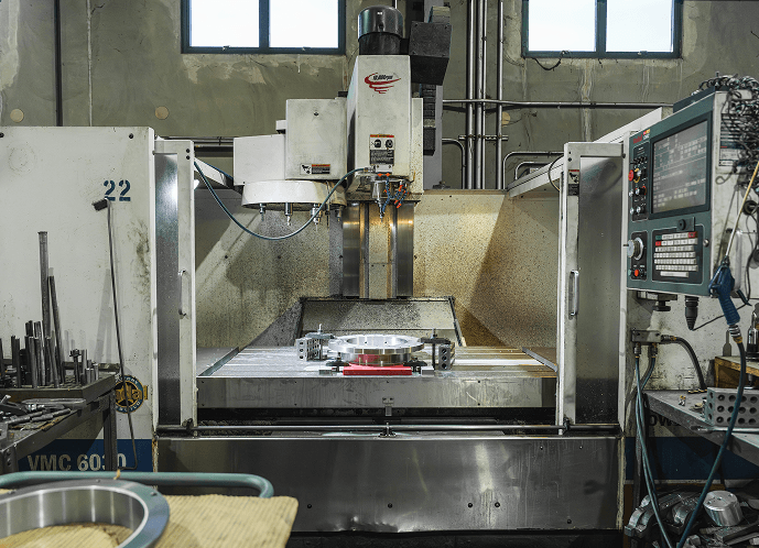 A large Willson CNC milling machine with a circular metal workpiece clamped on its bed, showing the machine's interior and control panel in an industrial workshop.
